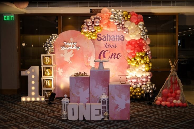 Pink and gold first birthday decoration with balloon garland, plinths and marquee light